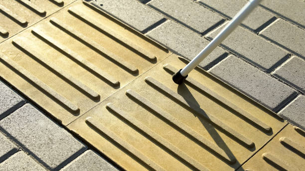 Blind person using white cane on straight tactile tiles to navigate road